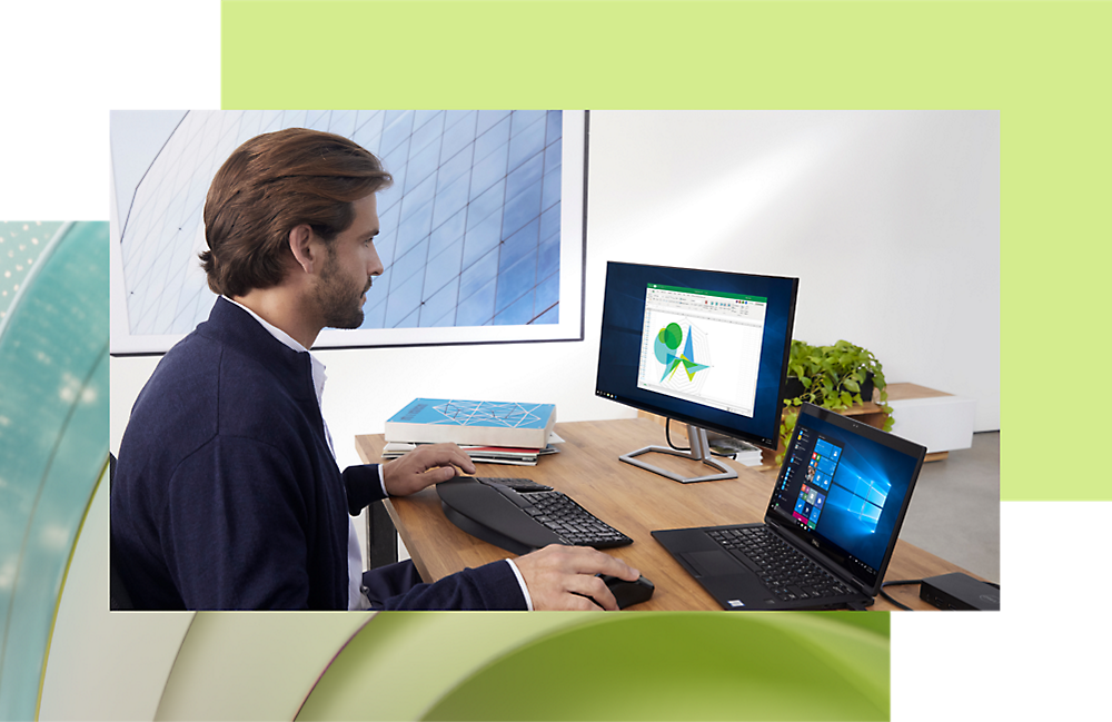 Man working on a desktop and laptop at a modern office desk, analyzing data on a screen with graphical charts.