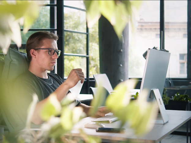 Un homme avec des lunettes se trouve à un bureau, tenant un morceau de papier, entouré d’une bande passante, 