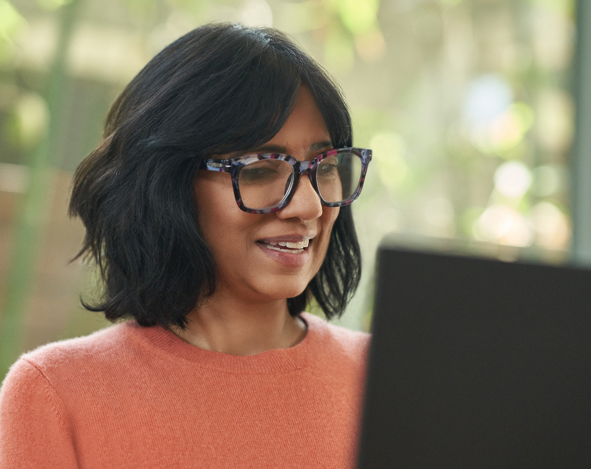 Femme avec des lunettes souriantes et travaillant sur son ordinateur portable