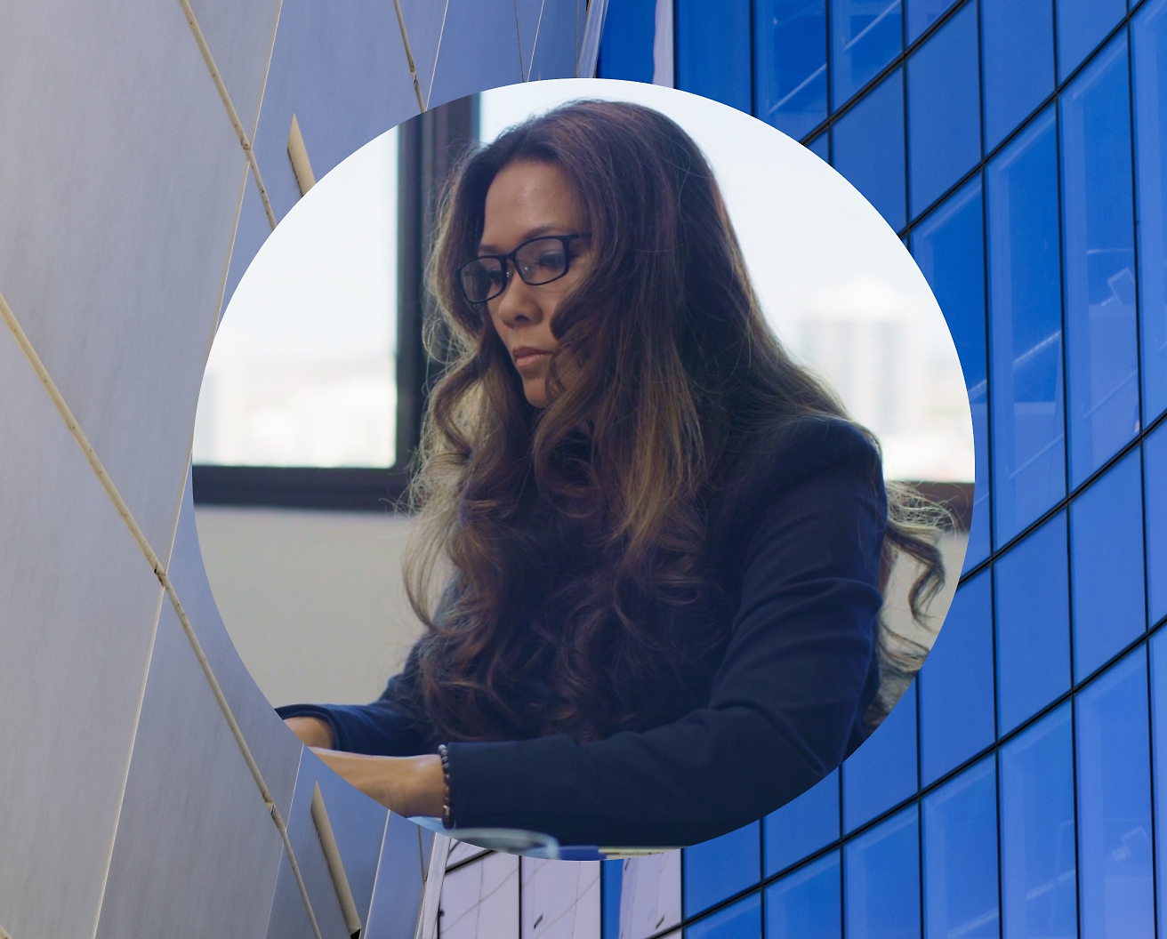 A woman working on her laptop wearing spectacles and background image set as glass building