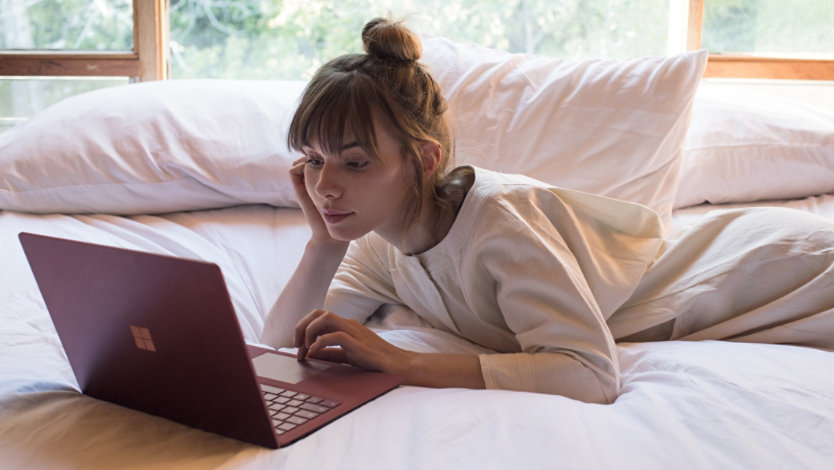 Eine Frau mit einem Surface Laptop 5 auf dem Bett. 