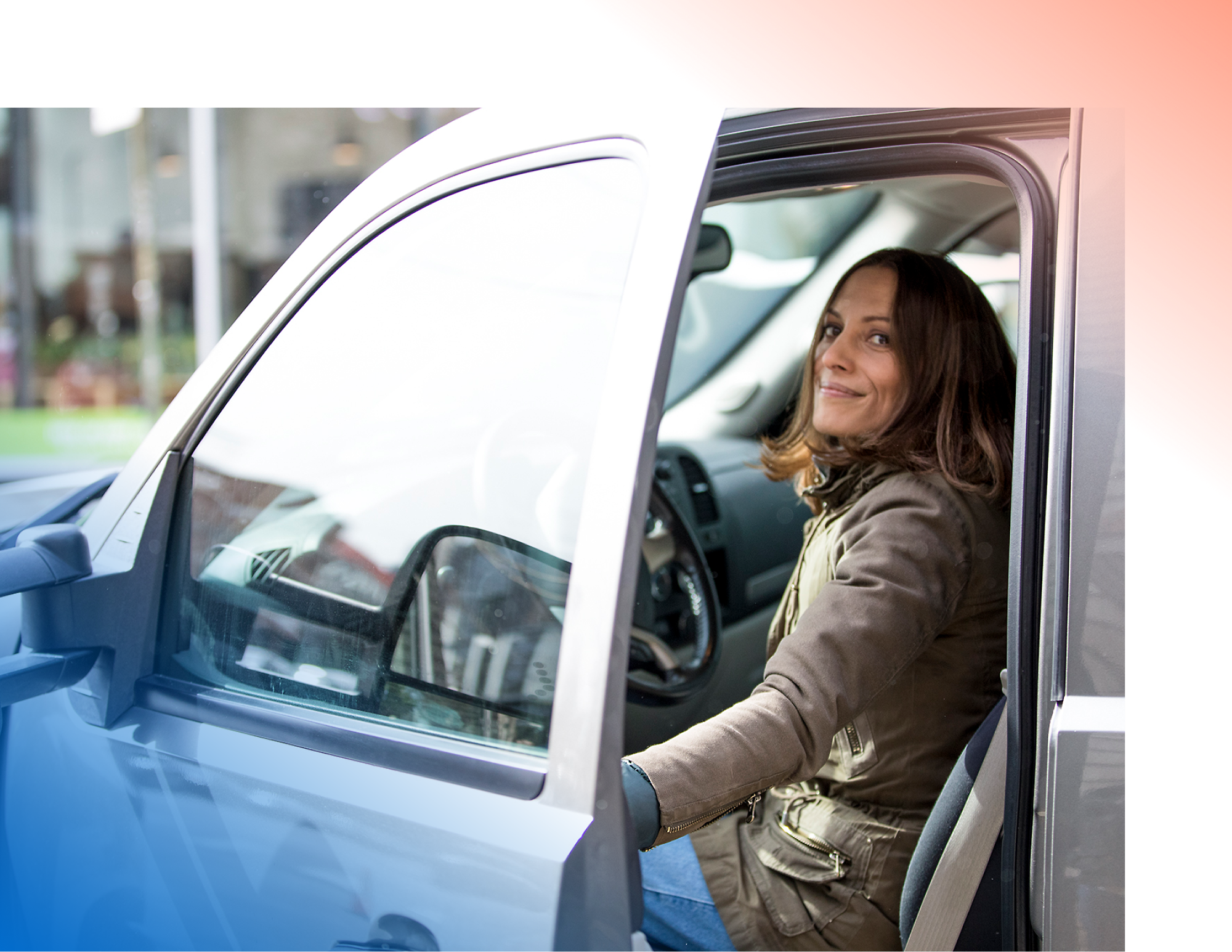 A person sits in the driver's seat of a car, smiling, with the driver's door open.