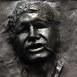 Close-up of a visage of Han Solo, frozen in a brown metal carbonite.