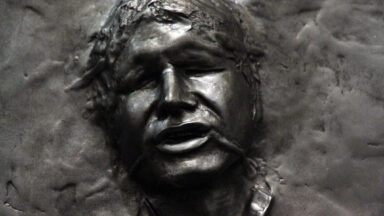 Close-up of a visage of Han Solo, frozen in a brown metal carbonite.