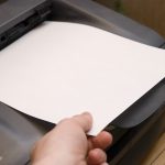 Someone touching a piece of paper that's sitting in a printer