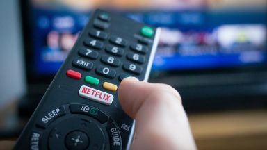 A person's hand holding a TV remote control with a Netflix button.