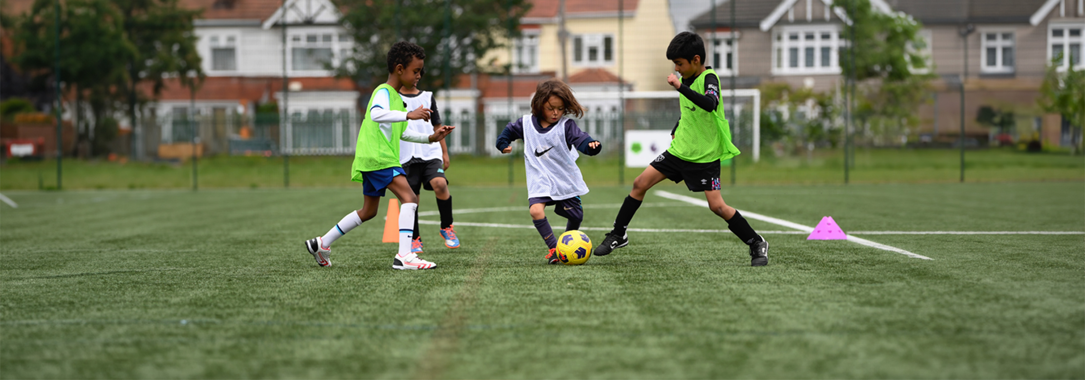 A young player runs forward with the ball, looking to dribble between two opponents, with one opponent trying to tackle him.