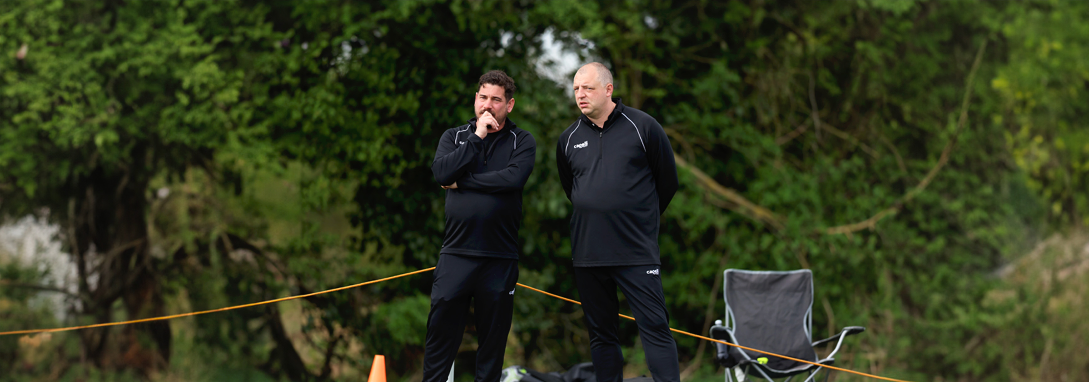 Two coaches chat with each other on the side of the pitch during matchday.