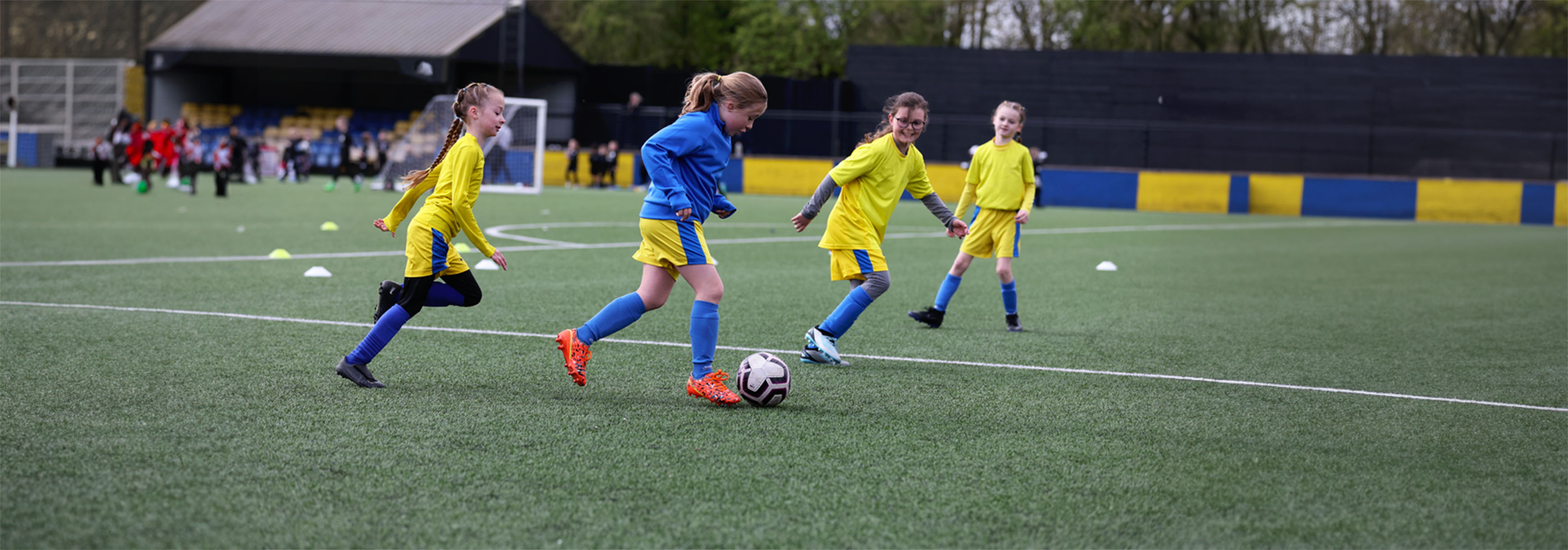 A young girl runs forward with the ball and towards the box, with three opponents near her, during a training drill.