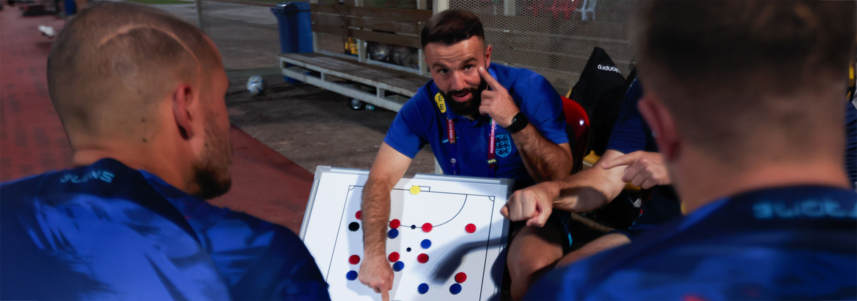 Coach with the England deaf football team points at a tactics board and uses his other hand to point to his eye.