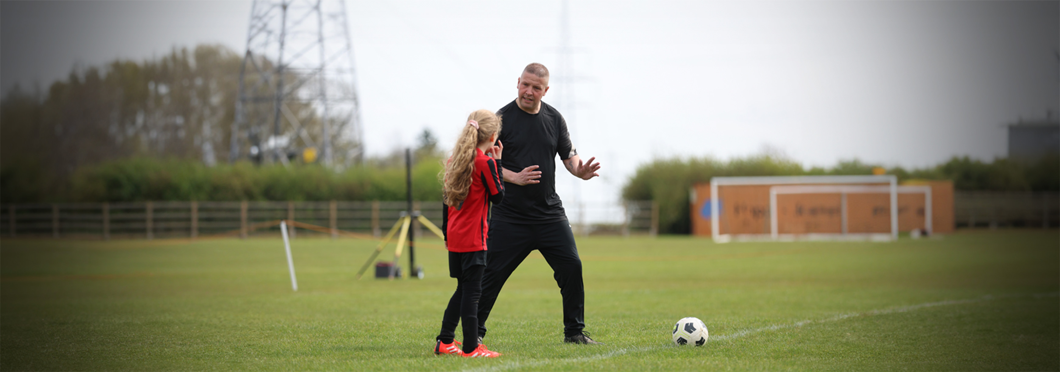 A coach talks to a player at the side of a pitch.