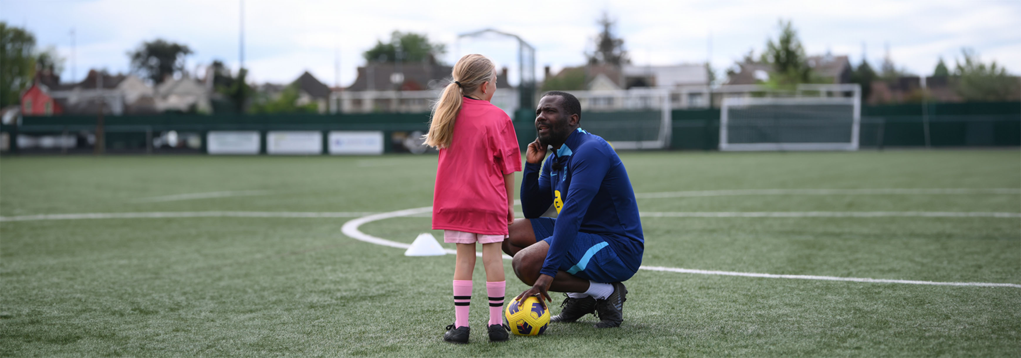 An FA coach squats down to listen to a young player during training on an outdoor 3G pitch.