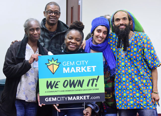 Group of smiling people holding a sign celebrating the grand opening of a new cooperative market in Dayton, OH. The employee-owned store received financing from Finance Fund Capital Corporation.