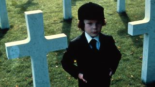 Harvey Spencer Stephens as Damien Thorn standing in a graveyard during The Omen.