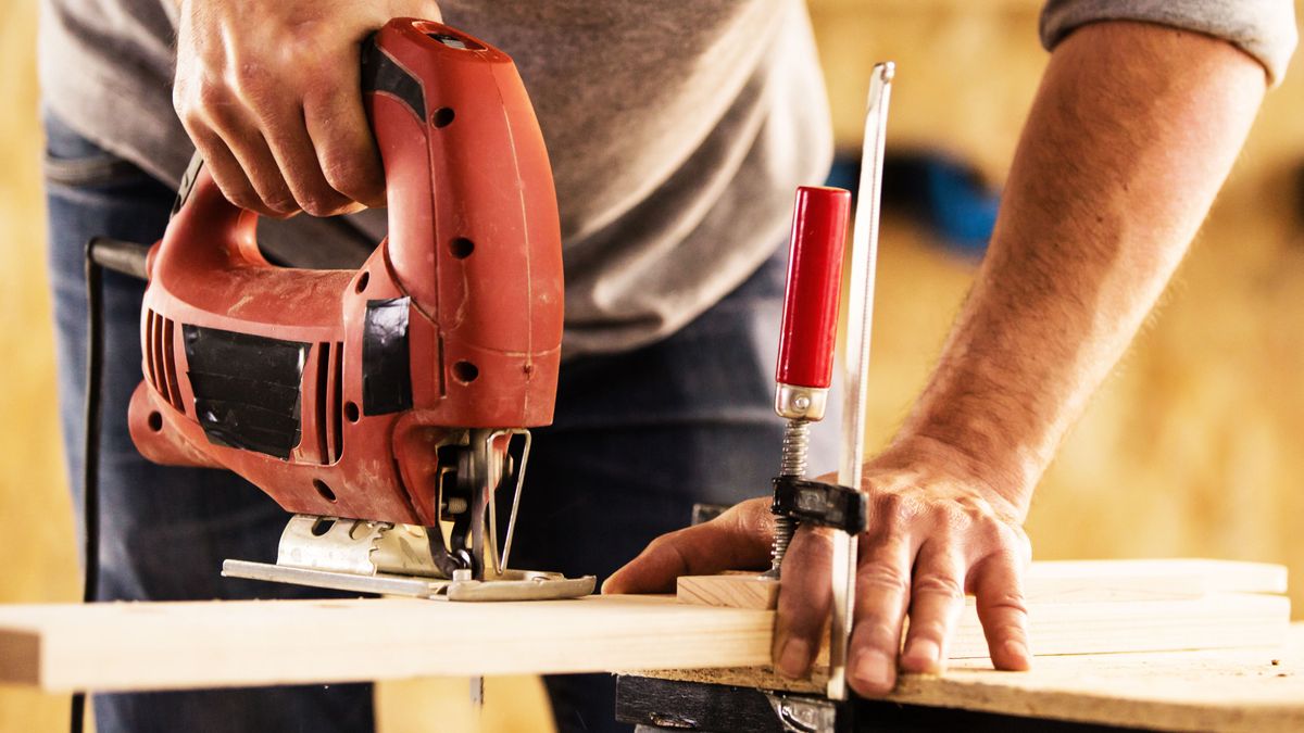 Person using a red jigsaw power tool to cut wood