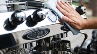 Person's hand wiping front of coffee maker with cloth