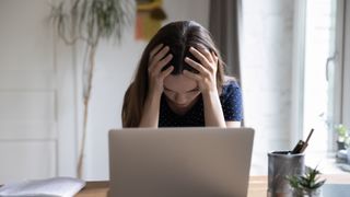 Frustrated unhappy laptop user girl touching head at work table with computer