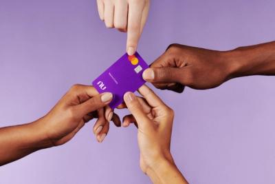 Quatro mãos seguram um cartão MasterCard roxinho do Nubank