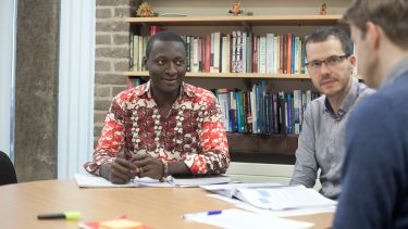 PhD student in meeting with supervisors in office with bookshelf