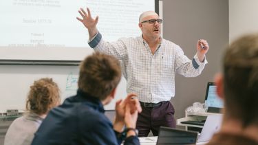 Politics professor explaining something to a class in front of a projector