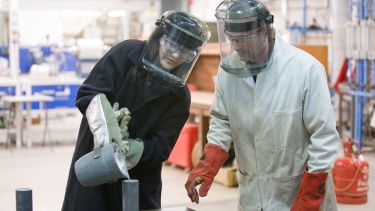 Materials Science student wearing protective clothing pouring from a jug