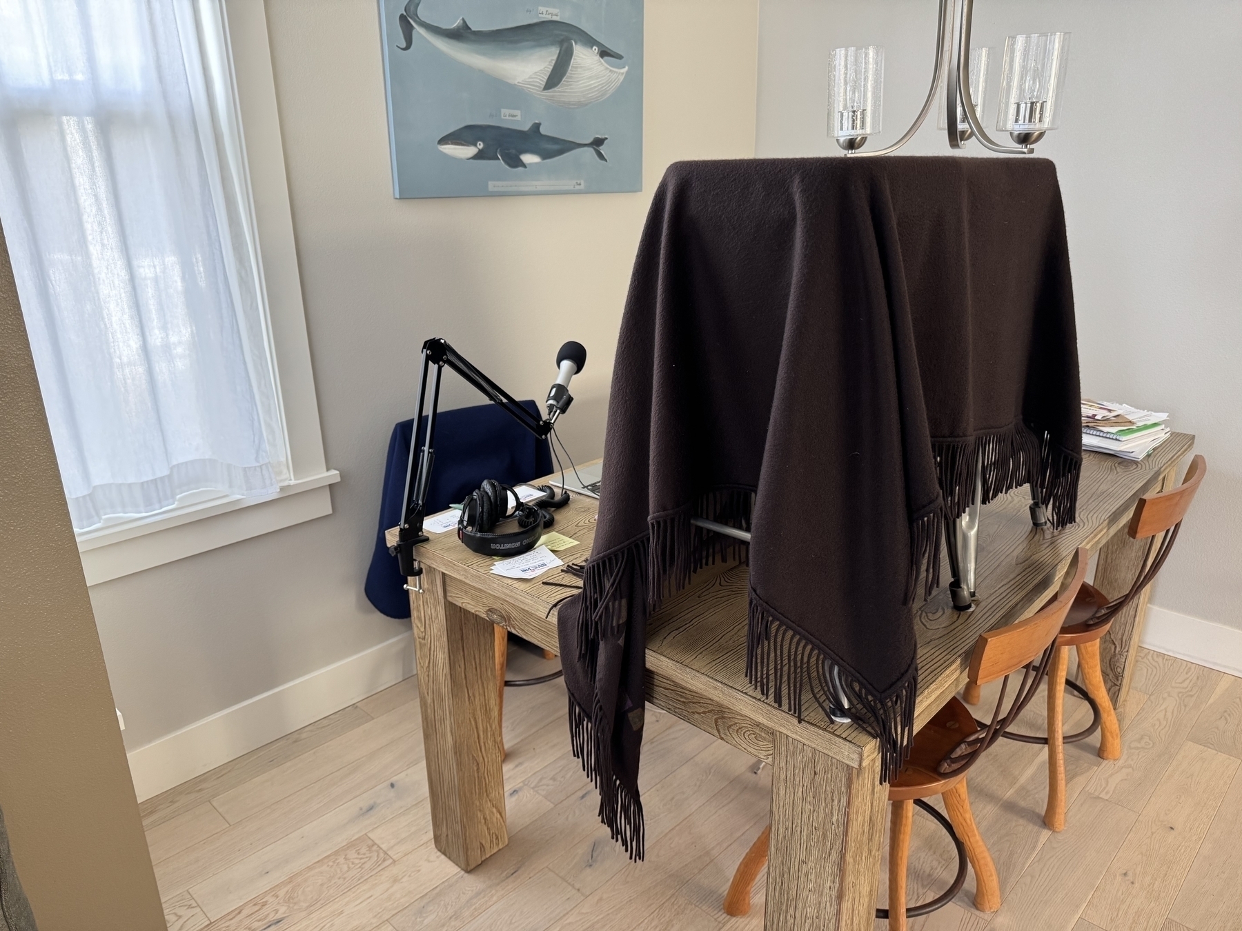 Large table with two stools on top, covered with a throw, computer and microphone. Print of whales on the wall. 