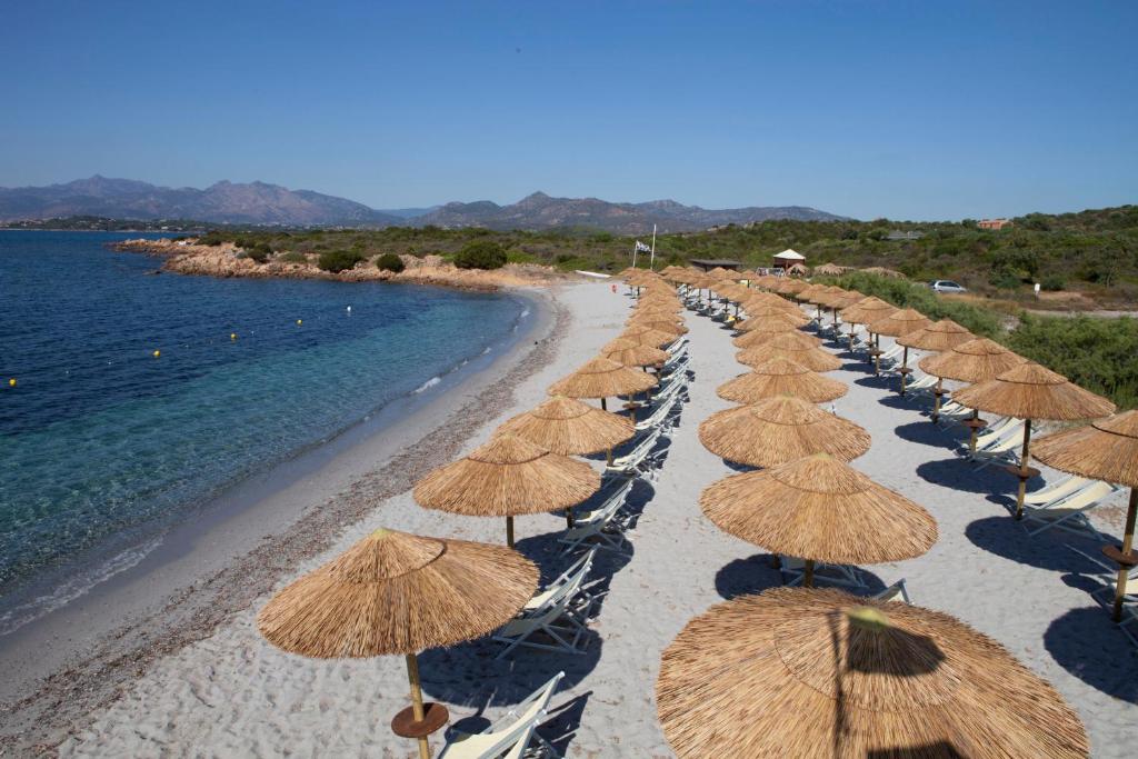 una fila de sombrillas de paja en una playa en Residence Baia Salinedda, en San Teodoro