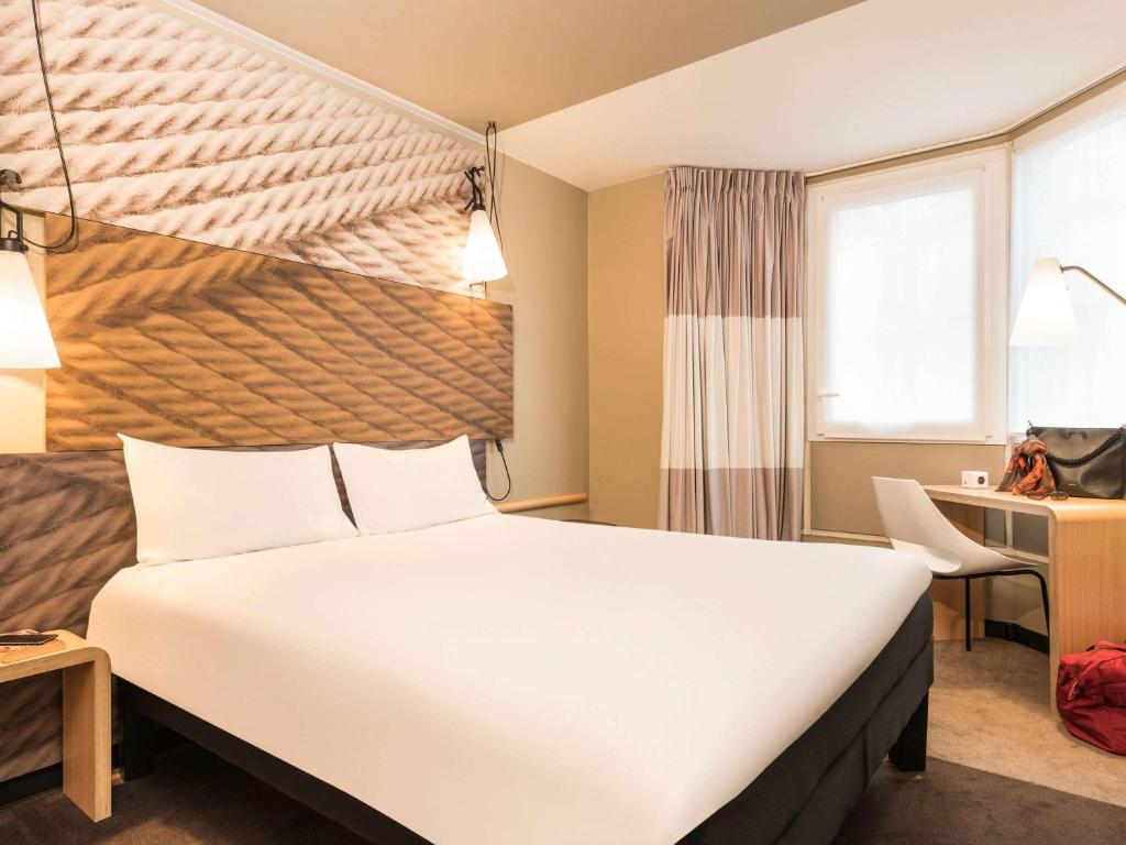 um quarto de hotel com uma cama grande e uma secretária em ibis Paris Gare du Nord Château Landon 10ème em Paris