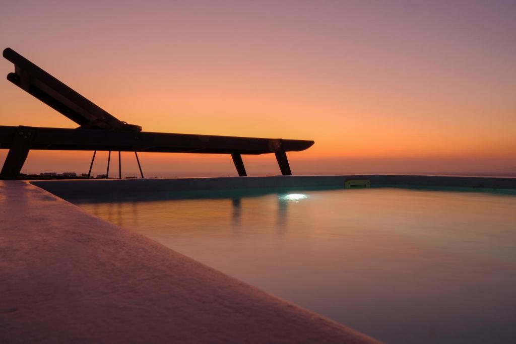 um banco sentado ao lado de uma massa de água ao pôr do sol em Aplada Suites em Oia