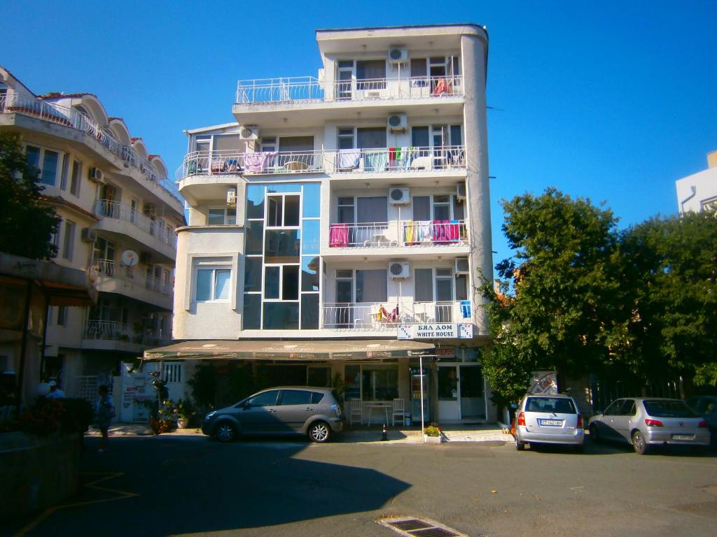 un edificio blanco alto con coches estacionados en un estacionamiento en Family Hotel White House, en Pomorie