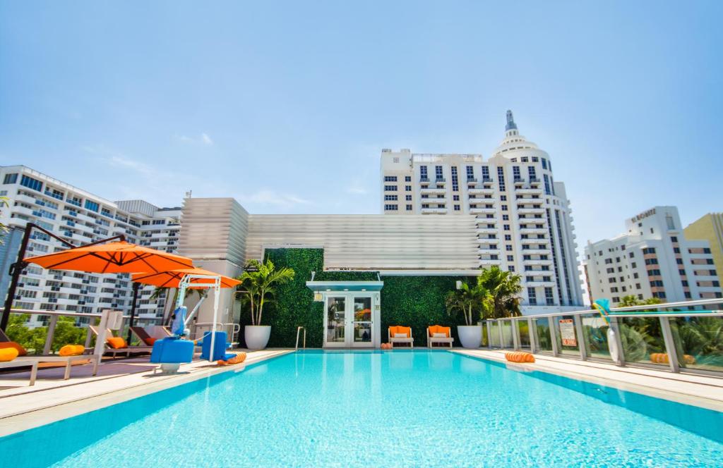 einen Pool mit Stühlen, einem Sonnenschirm und Gebäuden in der Unterkunft Berkeley Shore Hotel in Miami Beach