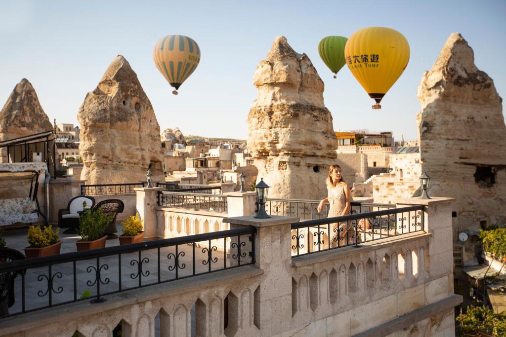 Eine Frau steht auf einem Balkon mit Heißluftballons in der Unterkunft Stone House Cave Hotel in Goreme