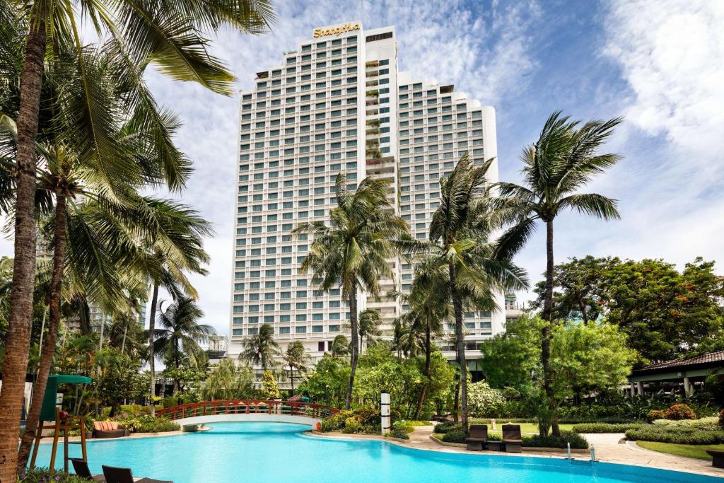 un grand bâtiment avec des palmiers en face d'une piscine dans l'établissement Shangri-La Jakarta, à Jakarta