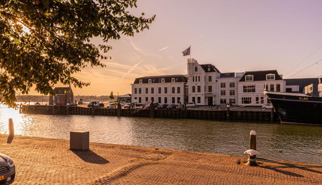 un grand bâtiment blanc à côté d'une étendue d'eau dans l'établissement Hotel Maassluis, à Maassluis