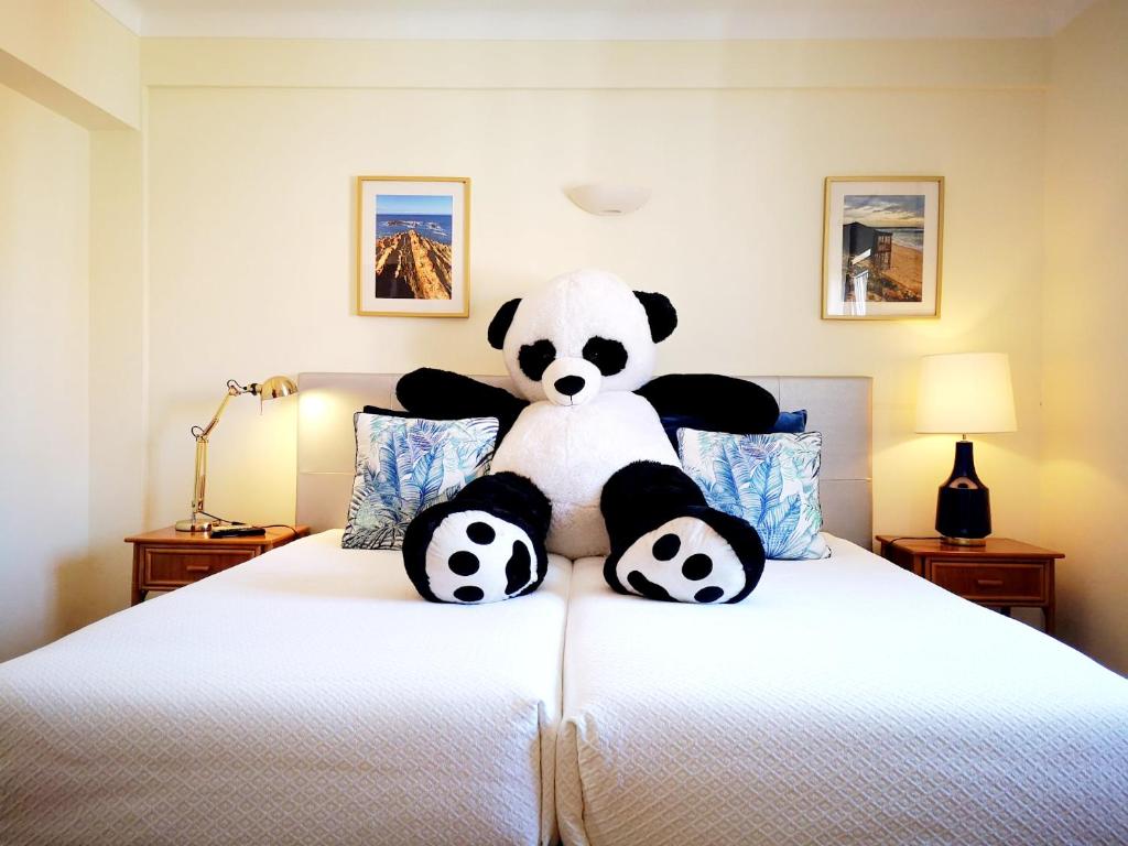 un oso panda de peluche sentado en la parte superior de una cama en The Blue Bamboo Hotel - Duna Parque Resorts & Hotels, en Vila Nova de Milfontes