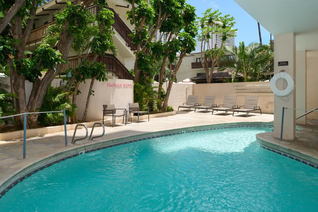 a swimming pool in a hotel with chairs and trees at Ilima Hotel in Honolulu