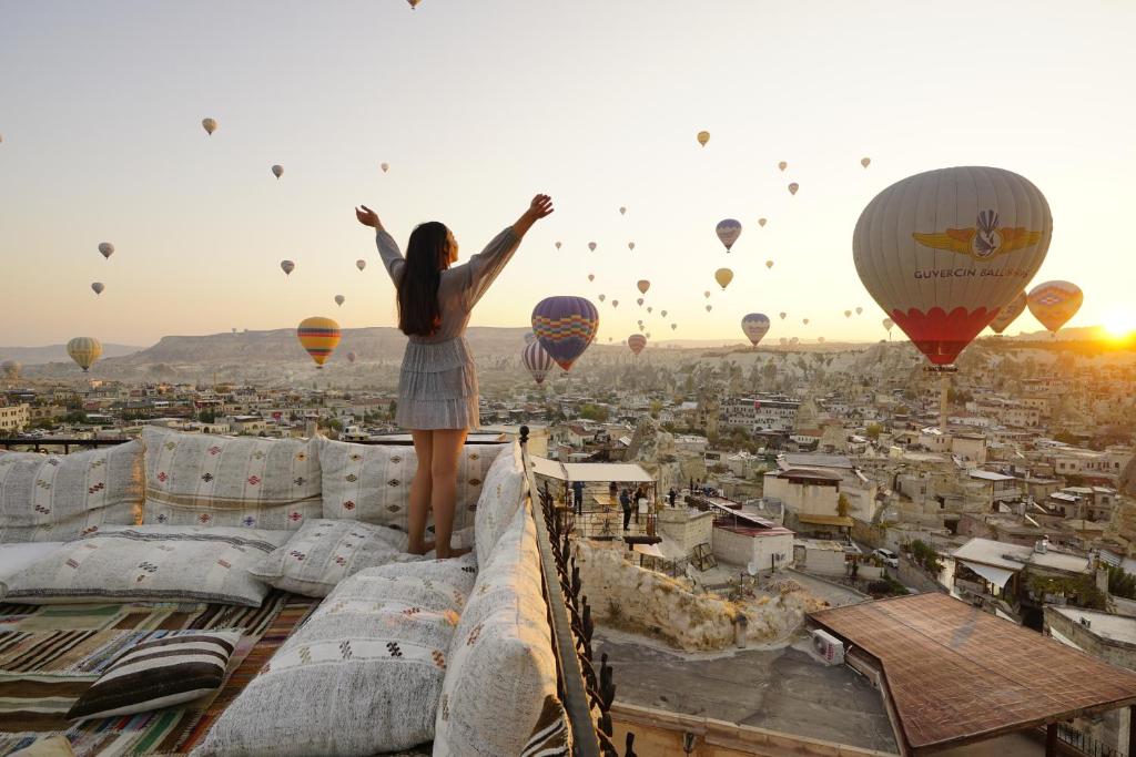 Une fille debout au sommet d'un bâtiment qui regarde des montgolfières dans l'établissement Tulip Cave Suites, à Gorëme