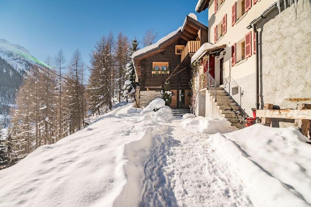 un sentiero coperto da neve di fronte a un edificio di "CHALET dei FIORI" room & apartment a Bedretto