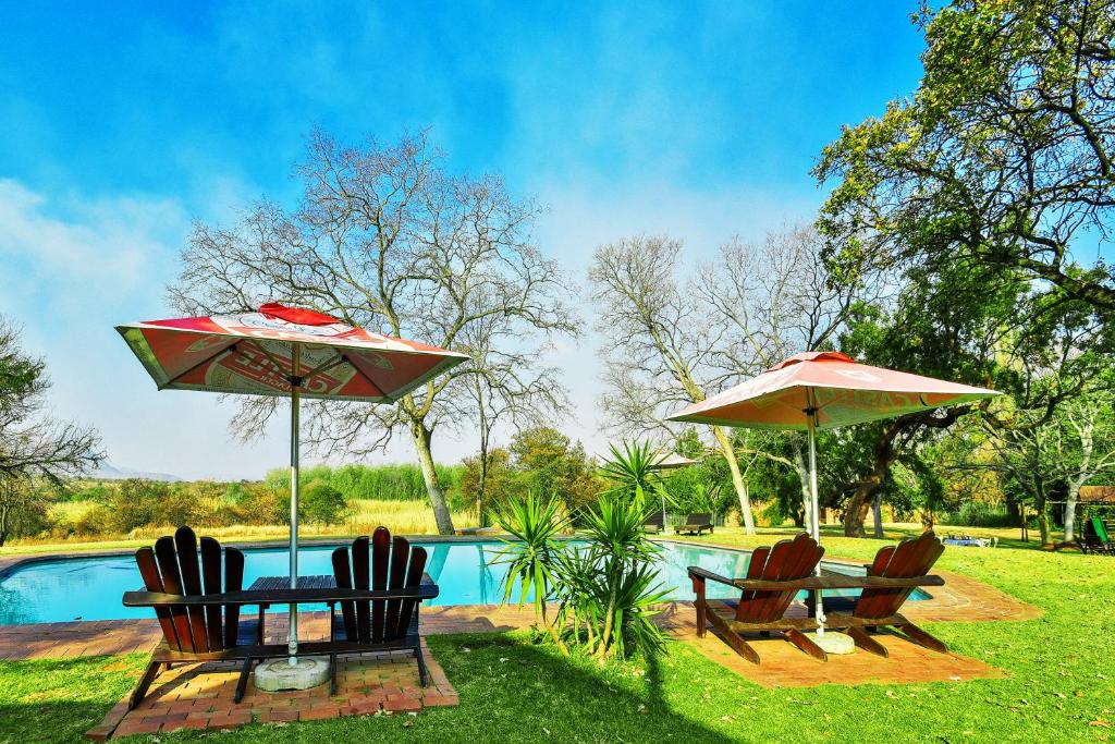 Dois guarda-sóis e cadeiras junto a uma piscina em The Venue Country Hotel & Spa em Hartbeespoort