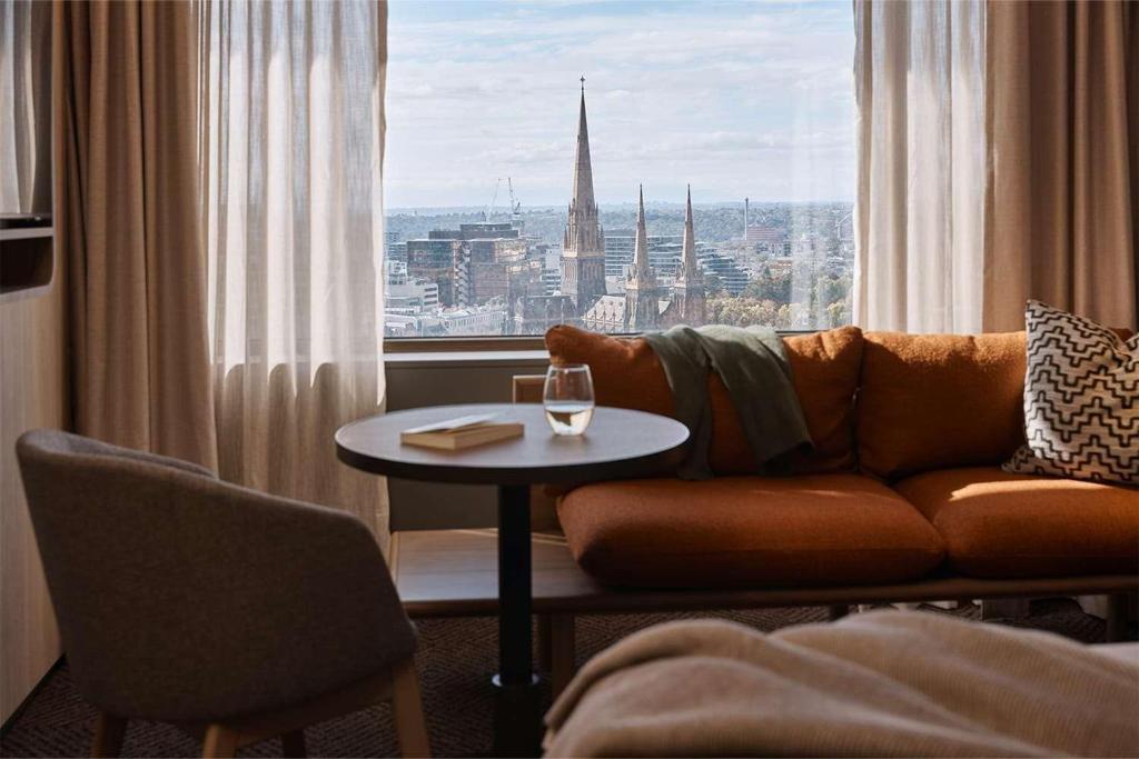 ein Wohnzimmer mit einem Sofa und einem Tisch mit einem Glas Wein in der Unterkunft Rydges Melbourne in Melbourne