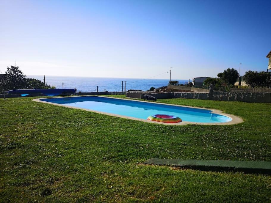 una piscina in un campo con l'oceano sullo sfondo di Banana House a Baiona