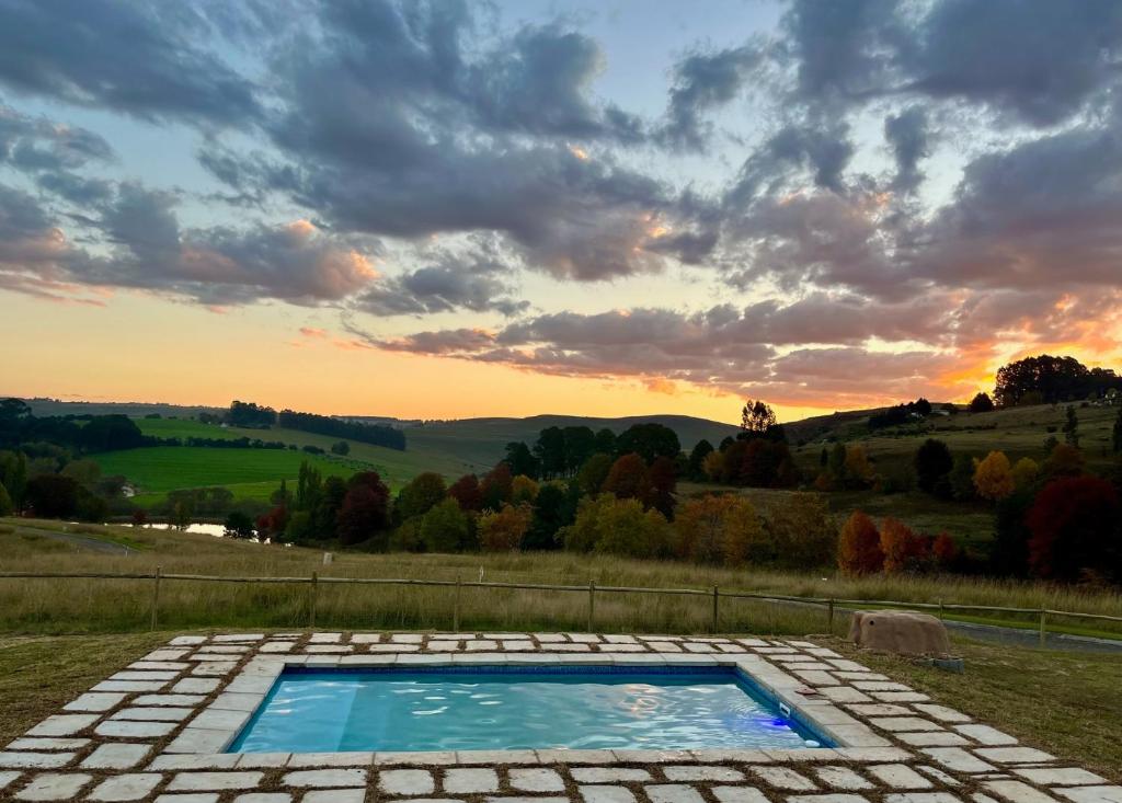 uma piscina num relvado com um pôr-do-sol ao fundo em Lalamanzi Trout Cottage - Solar Powered em Underberg