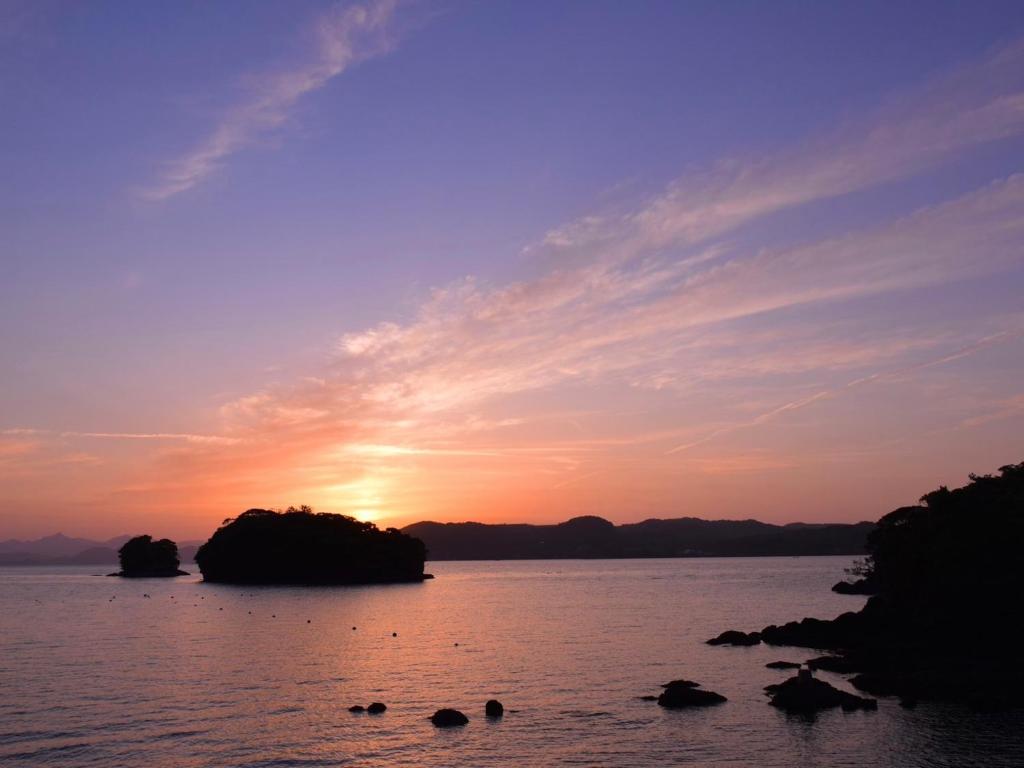 un coucher de soleil sur une étendue d'eau avec des rochers dans l'établissement ホワイトハウス, à Sasebo