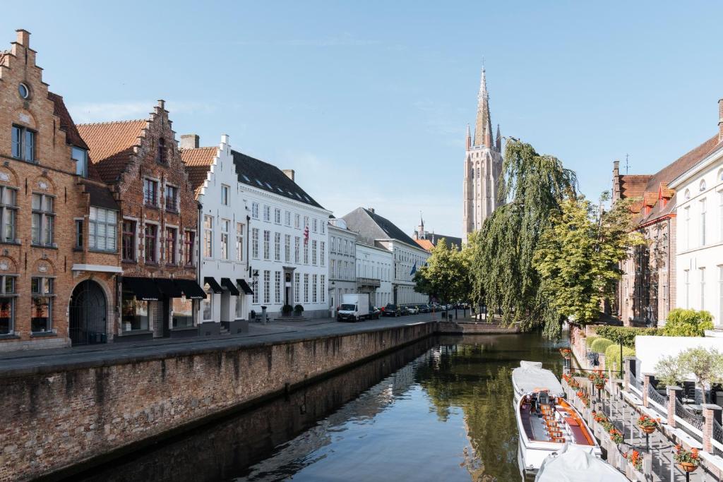 un canal en una ciudad con edificios y una iglesia en De Tuilerieën - Small Luxury Hotels of the World en Bruges