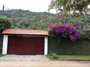 un garaje rojo y blanco con un arbusto con flores púrpuras en Casa Aconchegante - Circuito Teresópolis Friburgo en Teresópolis