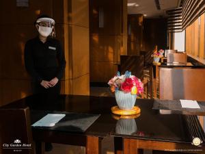 un hombre con una máscara facial y un jarrón de flores en una mesa en City Garden Hotel Makati en Manila