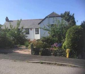 a white house with bushes and flowers in front of it at Ferney Croft in Saint Erth