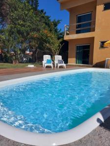 una piscina con 2 sillas y una casa en Pousada Mirante de Areia-Itaúnas en Itaúnas