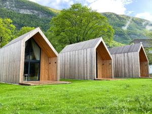 tres edificios de madera en un campo con montañas en el fondo en Cabino - Fresh Air Resort en Bovec