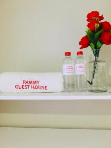 uma prateleira com duas garrafas e uma toalha e um vaso com flores em Pammy Guest House em Richards Bay